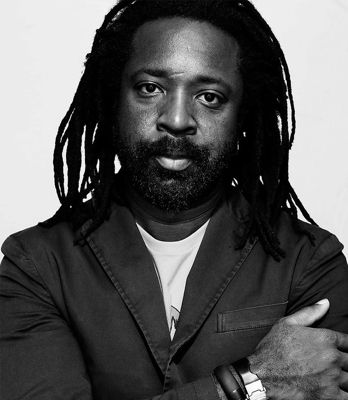 Portrait en noir et blanc d'un homme noir, les bras croisés, dread locks